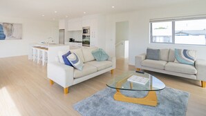 Un salon moderne avec deux canapés, une table basse en verre et une cuisine en arrière-plan.