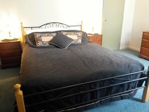A bed with a metal frame, a dark bedspread, and two decorative pillows. There are wooden nightstands with lamps on either side of the bed. - Ezy Walk - Blenheim Holiday Home (Blenheim)