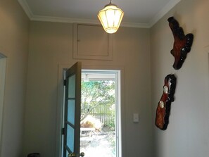 A room with a door leading to a backyard, a hanging light fixture, and two wall-mounted objects. - Ezy Walk - Blenheim Holiday Home (Blenheim)