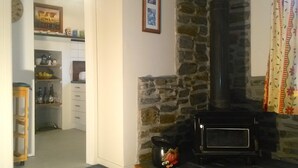 Een gezellige woonkamer met een stenen open haard, een keuken met planken en een koelkast, en een deur naar een andere kamer.