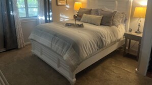 A bedroom with a large bed, two bedside tables with lamps, a window with curtains, and a framed picture on the wall. - Historic Home/Apt... (Tarpon Springs)