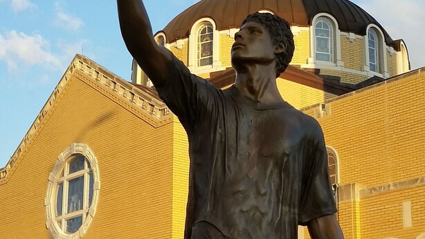 A statue of a man holding a trophy in front of a building with a dome and arched windows. - Historic Home/Apt... (Tarpon Springs)