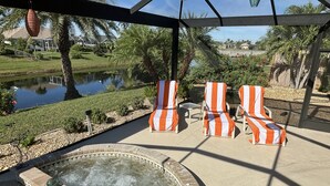 Un espace piscine doté de chaises longues, d’un jacuzzi et offrant une vue sur un lac et des palmiers.