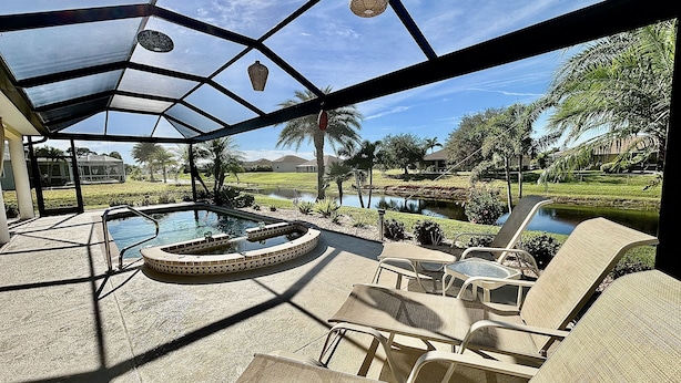 Un espace extérieur abrité comprenant une piscine, des chaises longues et une vue sur un jardin aménagé et sur des maisons situées au loin.