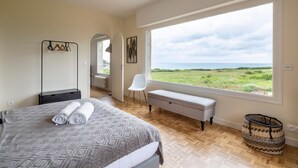 A bedroom with a large window, a bed with rolled towels, a bench, a chair, and a basket. - Le Sémaphore - Maison avec sauna Vue mer (Cancale)