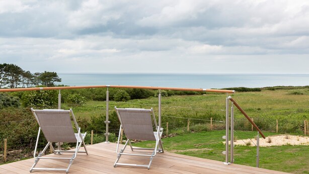 A deck with two metal chairs and a wooden railing overlooking a grassy area and the sea. - Le Sémaphore - Maison avec sauna Vue mer (Cancale)