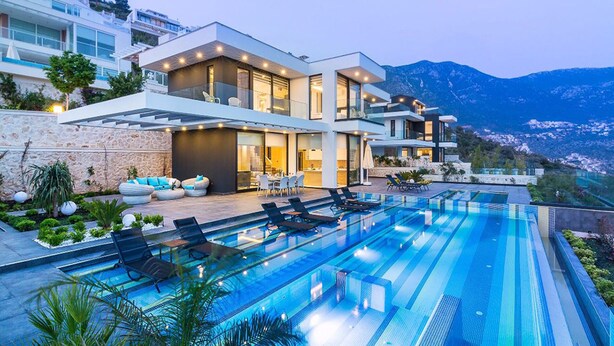 Eine moderne Villa mit großem Swimmingpool, Sitzgelegenheiten im Freien und Blick auf die Berge.