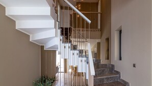 Eine moderne Treppe mit weißer Geländer und Glastrennwand, die zu einem Anlaufpodest im zweiten Stock mit Blick ins Innere führt.