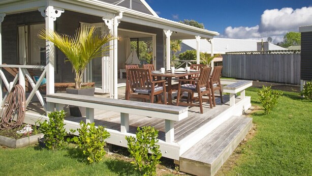 Un patio techado al aire libre con una mesa y sillas para comer, rodeado por una terraza de madera y pequeñas plantas.
