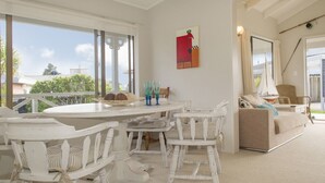 Un salón amplio con una mesa redonda para comer rodeada de sillas blancas, un sofá color beige y un ventanal con vistas al exterior.