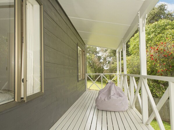 A covered porch with a white railing, a grey wooden wall, and a beige bean bag chair. - Best at The Beach - Whangamata Holiday Home (Whangamata)