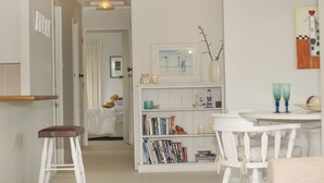 Una habitación acogedora con una estantería blanca, una pequeña mesa de comedor con sillas y un banco blanco.