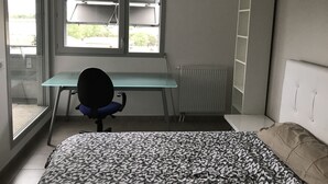 A bedroom with a bed, a desk, and a chair. There is a window with blinds, a radiator, and a wardrobe. - Apartment bayonne T2 (Bayonne)