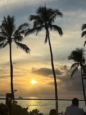 A sunset view with palm trees and a person seated at a table. -   Maui Eldorado, Beach Cabana, Snorkel Black Rock, Walk to Whalers  (Kaanapali)