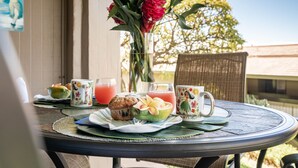 Une table dressée avec un muffin, un verre d’une boisson rose, un verre de jus d’orange, une assiette avec un fruit vert et une tasse à motifs floraux.