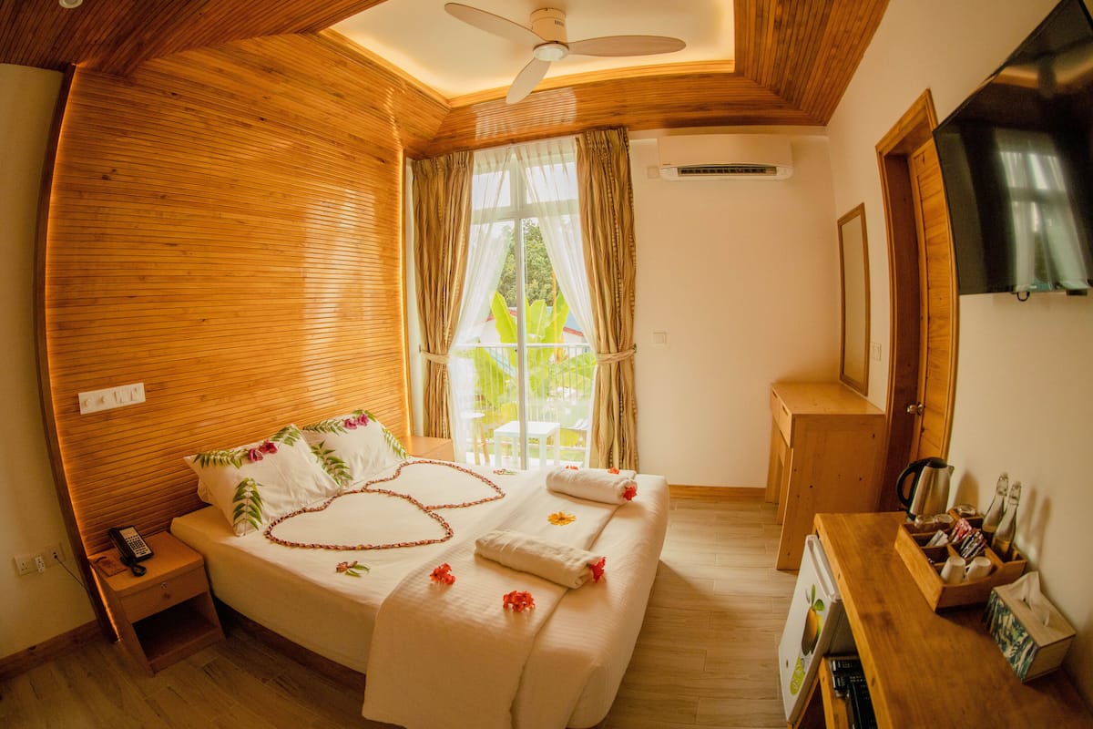 Une chambre avec un plafond en bois, un lit recouvert d’une literie à motifs floraux, une table de chevet avec un téléphone et une petite armoire en bois contenant des bouteilles.
