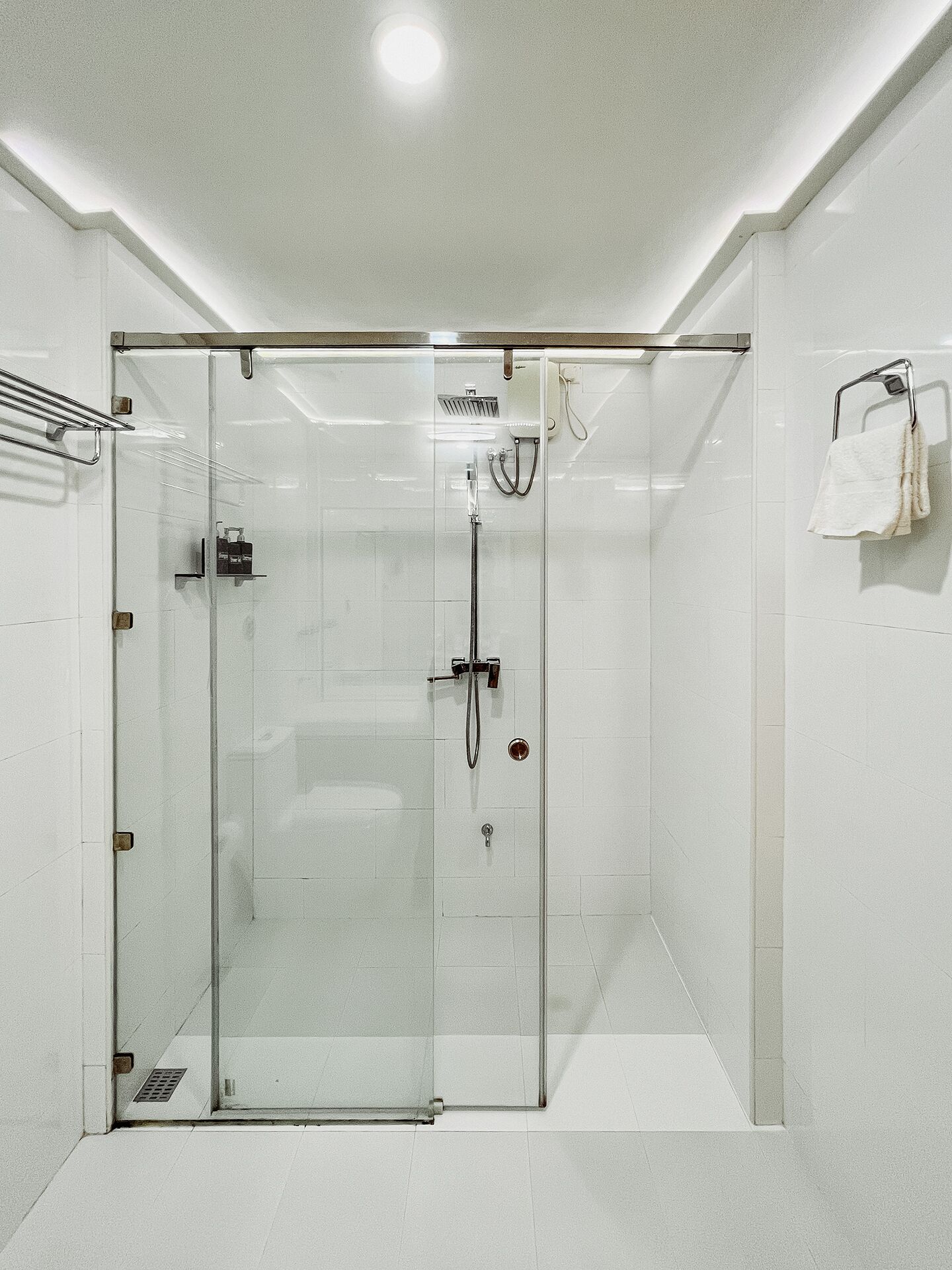 A modern shower room with a glass door, a handheld showerhead, a wall-mounted towel rack, and a built-in bench.