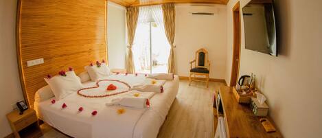 A hotel room with a large bed, a wooden ceiling, a TV, and a desk with a chair.