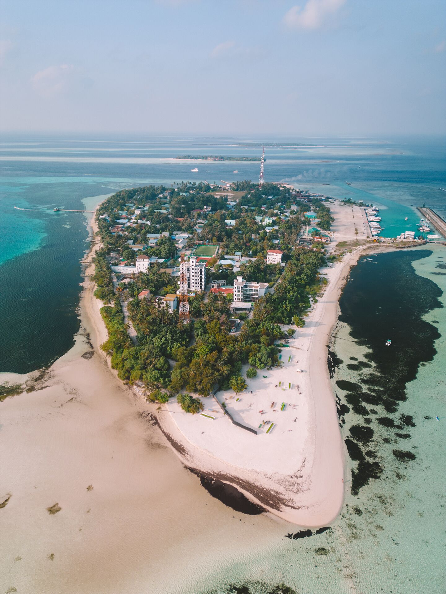 Une vue aérienne d’une station balnéaire, avec un ensemble de bâtiments au centre, entourés d’une végétation luxuriante et bordée d’une plage de sable.
