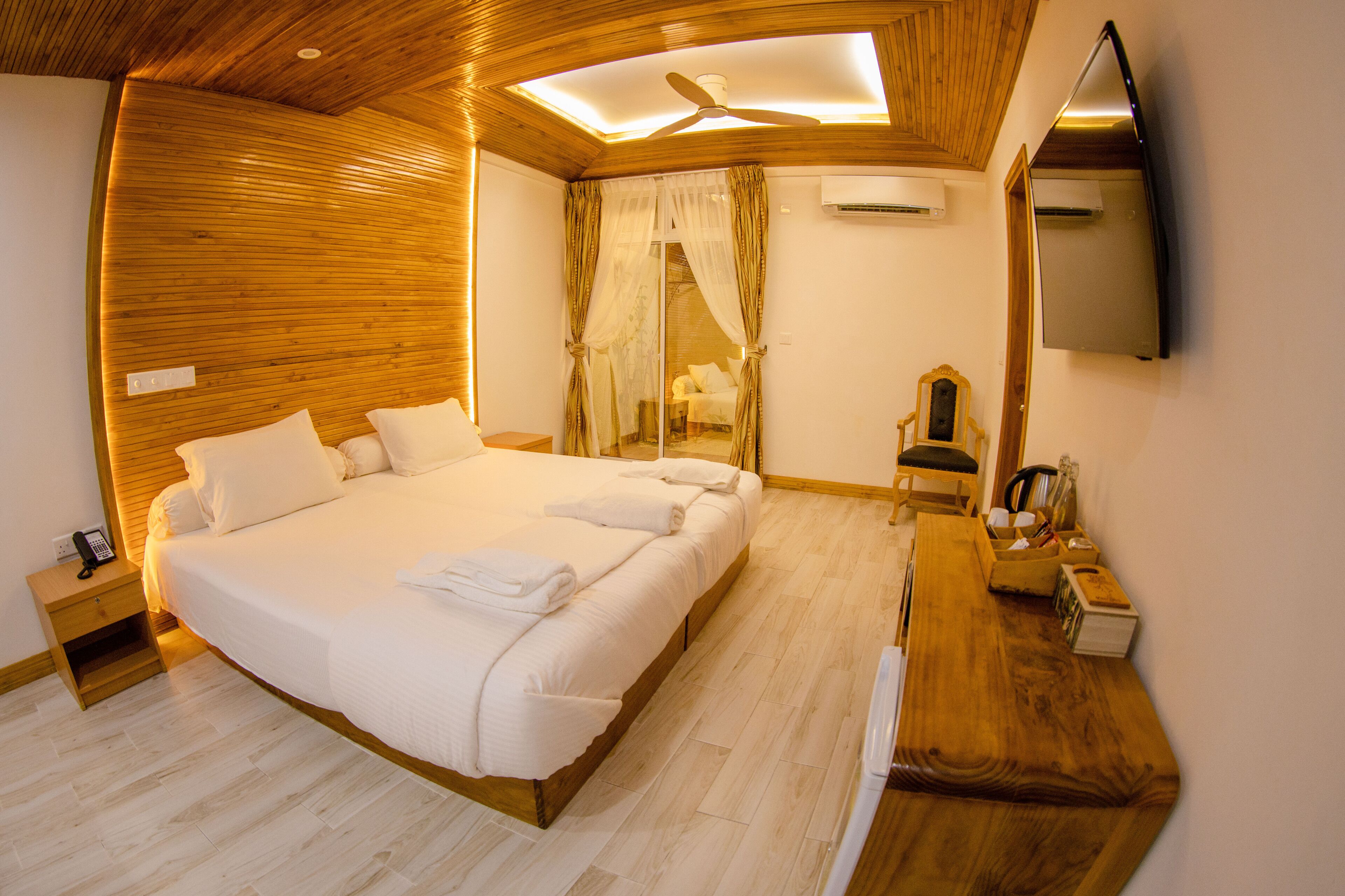 Une chambre avec un grand lit, une tête de lit en bois, une table de chevet avec un téléphone, un banc en bois et un miroir au mur.
