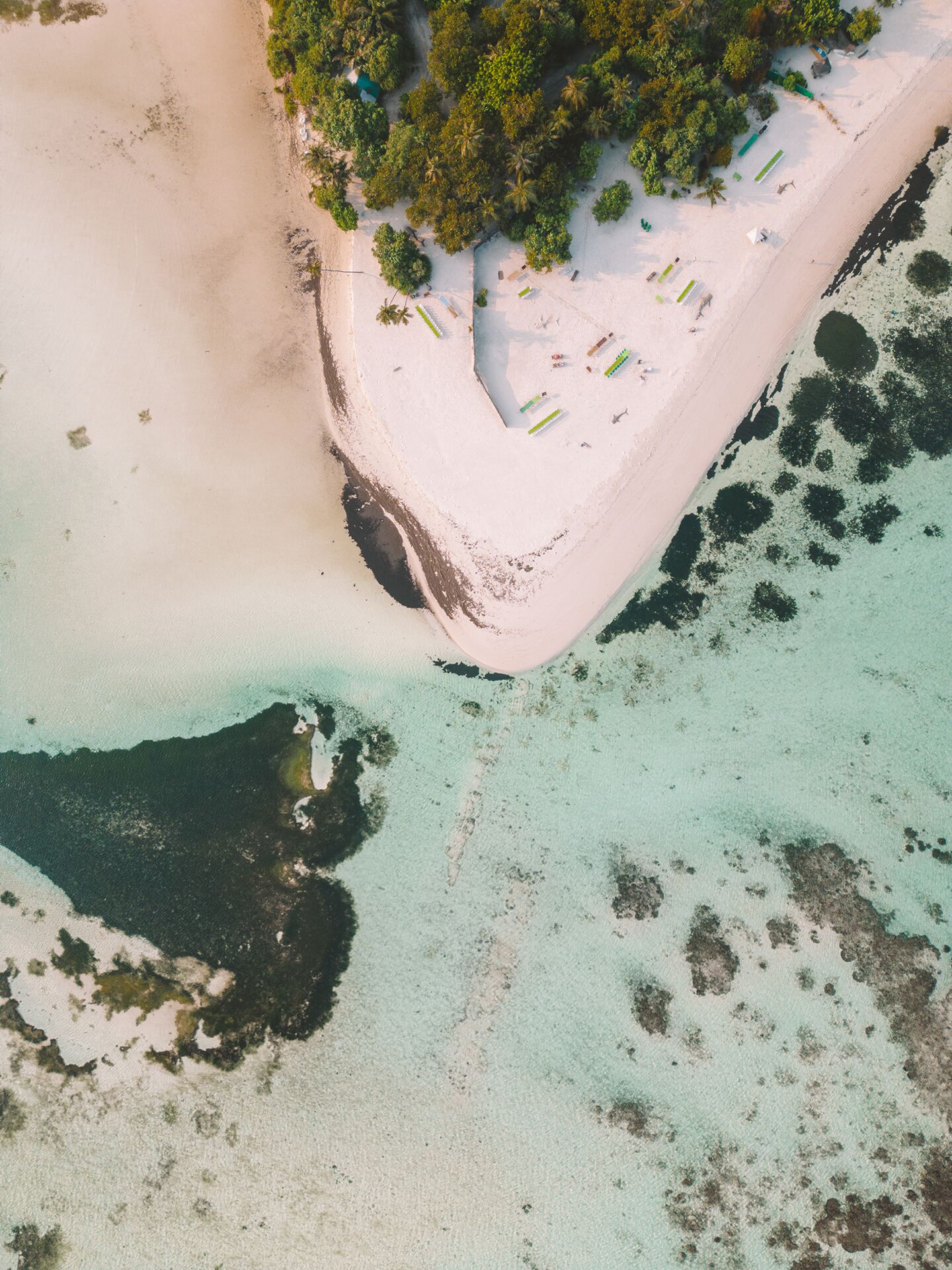 An aerial view of a beach with clear turquoise waters, a sandy shore, and a small cluster of beach umbrellas.