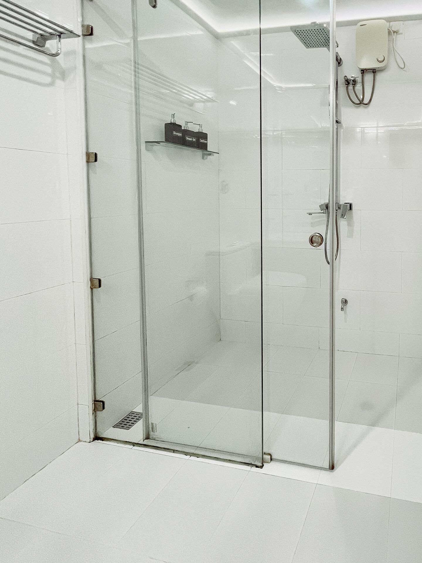 Een moderne badkamer met een douchecabine van glas, witte betegelde wanden en een zichtbare douchekop.
