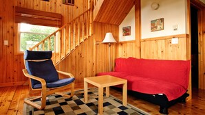 Ein Holzinnenraum mit einem blauen Sessel, einem roten Sofa und einem Holztisch.