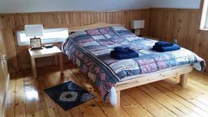 Ein Zimmer mit Holzwänden, einem Bett, einem Nachttisch, einer Lampe und einem Fenster.