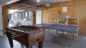 A room with a foosball table, ping pong table, and shelves with sports equipment. - Mountain Bike Manor - Spa Pool, Sleeps 8, Pets OK (Rotorua)