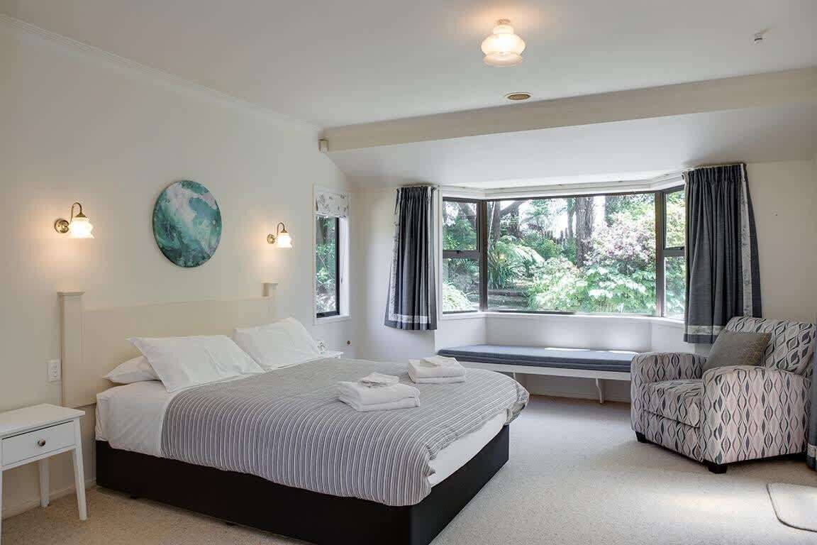 Une chambre à coucher avec un lit, une chaise, un banc et une grande fenêtre avec des rideaux.