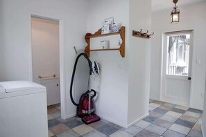 A laundry room with a washing machine, a vacuum cleaner, and a shelf with cleaning supplies.