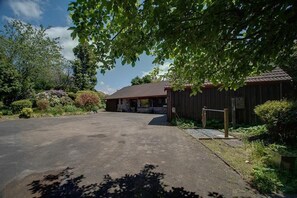 A building with a paved driveway leading to a wooden structure, surrounded by lush greenery and trees.