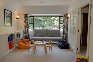 A cozy room with a sofa, a small table, and chairs. There is a window with curtains, a bookshelf, and a door.