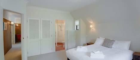 Quarto com uma cama grande, paredes brancas e uma luminária no teto. Guarda-roupas e um banheiro são visíveis ao fundo.