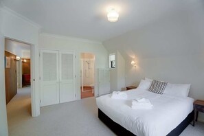 A bedroom with a large bed, white walls, and a ceiling light. There are closets and a bathroom visible in the background.