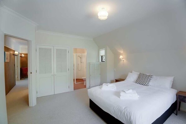 A bedroom with a large bed, white walls, and a ceiling light. There are closets and a bathroom visible in the background.