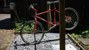 A red bicycle parked on a gravel path with a wooden post nearby. - Mountain Bike Manor - Spa Pool, Sleeps 8, Pets OK (Rotorua)