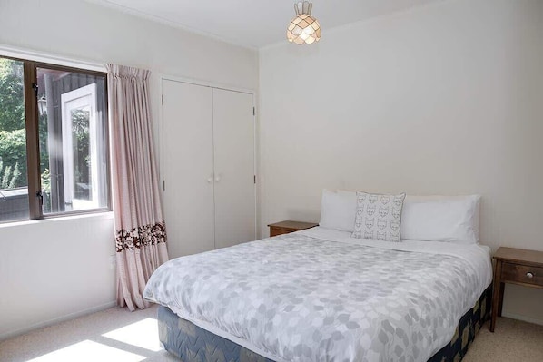 Ein Schlafzimmer mit Bett, Nachttischen, einem Fenster mit Vorhängen und einer Deckenleuchte.