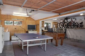 A room with a ping pong table, wooden cabinets, a television, and bicycles mounted on the wall.