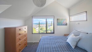 A bedroom with a large window, a dresser, a bed with pillows, and a ceiling light.