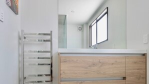 A modern bathroom with a large mirror, wooden vanity, and a towel rack.