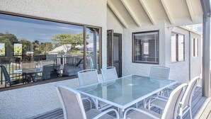 A glass-top table with four chairs, a sofa, and a window overlooking a deck area.