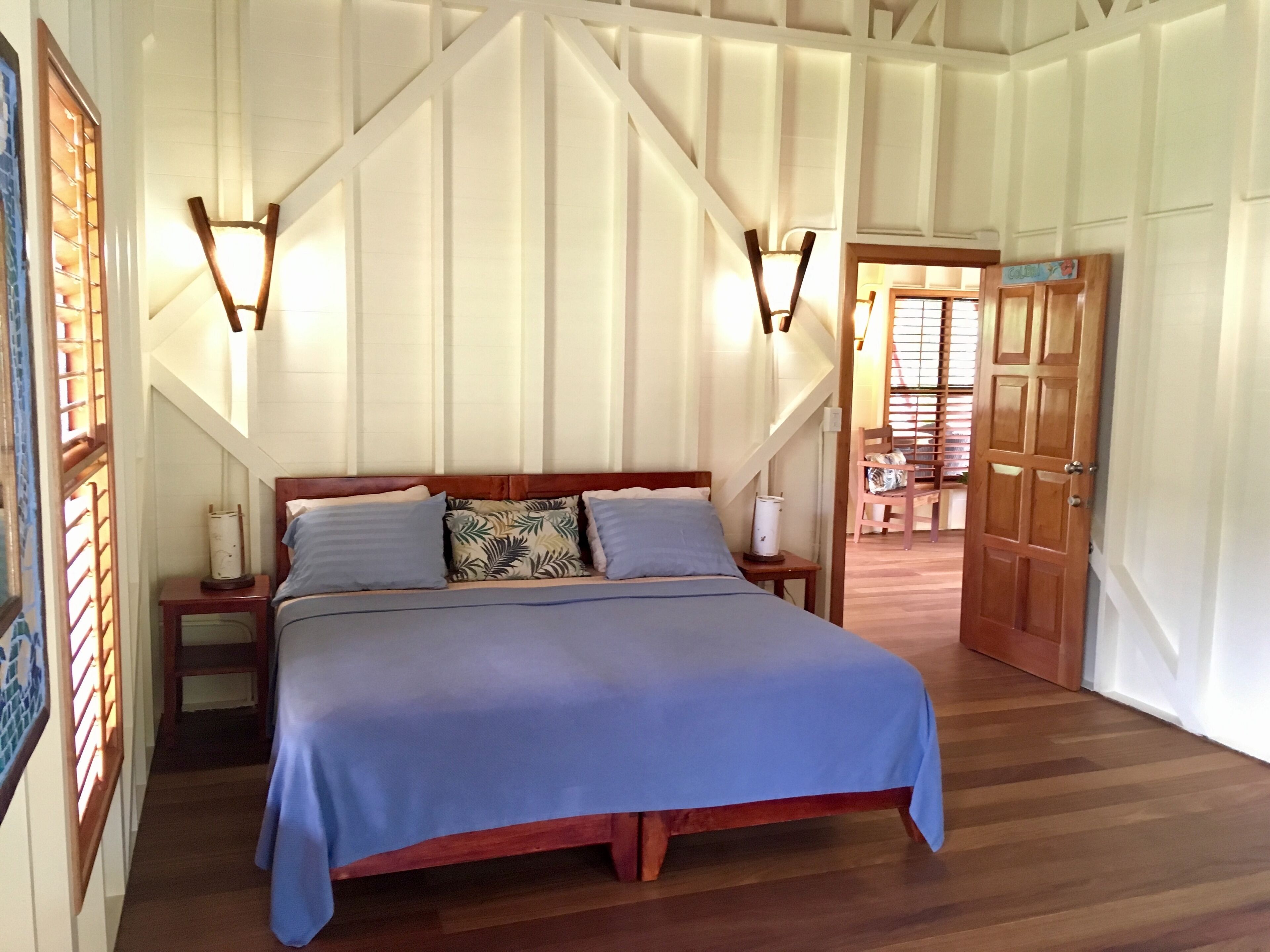 Una camera da letto con un letto grande, una testiera in legno, due comodini con lampade e una porta in legno che dà su un'altra stanza.
