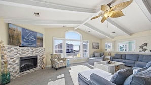 A living room with a fireplace, a ceiling fan, and a large window.