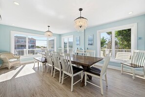 Ein Essbereich mit großem Tisch und Stühlen, großen Fenstern und einem Balkon mit weißen Geländern.