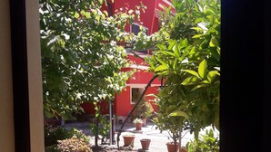 A view of a courtyard with potted plants and a red building in the background. - Domu de Palla (Bauladu)