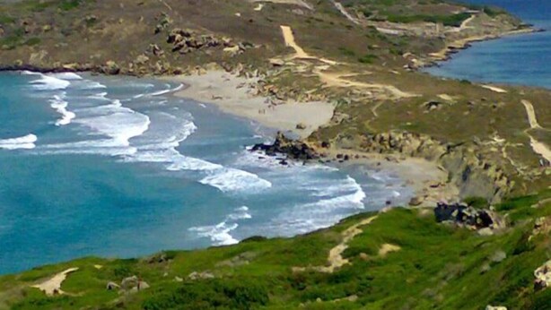 A coastal landscape with a beach, rocky terrain, and a path leading to a hilltop. - Domu de Palla (Bauladu)