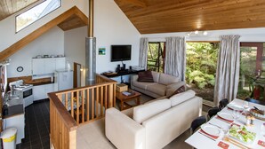 A spacious living area with a wooden ceiling, a sofa, a dining table set for four, and a kitchen in the background.