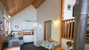 A compact kitchen with a stove, sink, and white cabinets. There's a table with a floral tablecloth and a vase with flowers.
