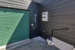 A corner of a building with a green garage door, a black wall with a white electrical box, and a metal pipe on the ground. - The Hideaway - Omaha Holiday Home (Omaha)